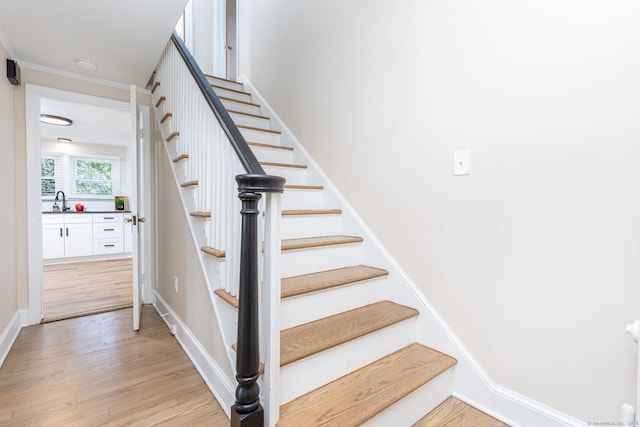stairs featuring wood finished floors and ornamental molding