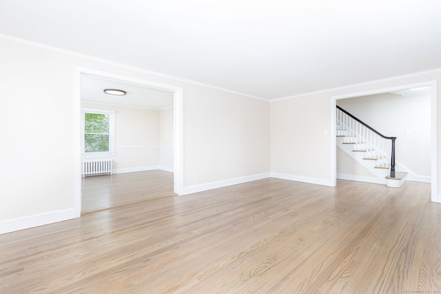 unfurnished living room with radiator heating unit, stairs, light wood-style floors, ornamental molding, and baseboards