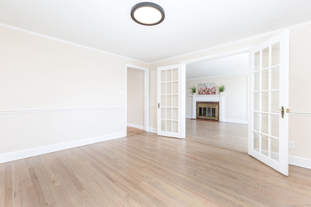 unfurnished living room with french doors, light wood-style floors, a brick fireplace, baseboards, and crown molding