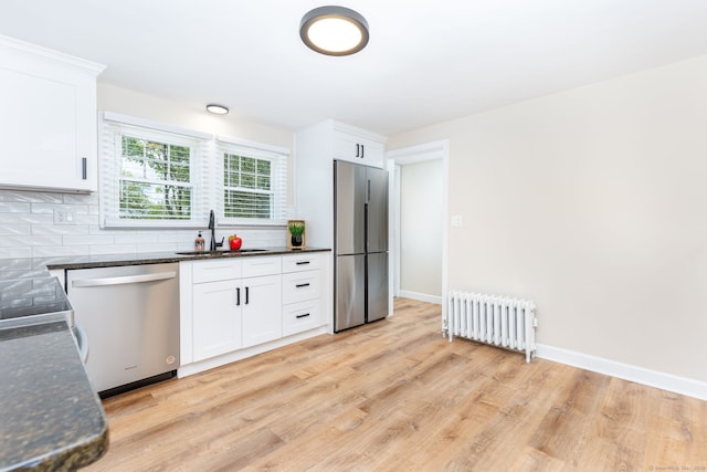 kitchen featuring radiator heating unit, stainless steel appliances, a sink, tasteful backsplash, and white cabinetry