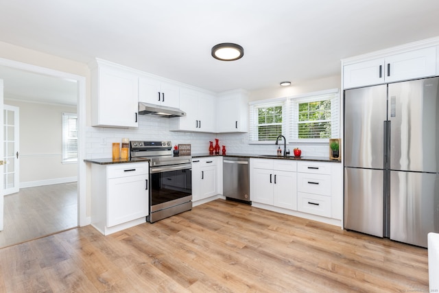 kitchen featuring stainless steel appliances, under cabinet range hood, light wood finished floors, decorative backsplash, and white cabinetry