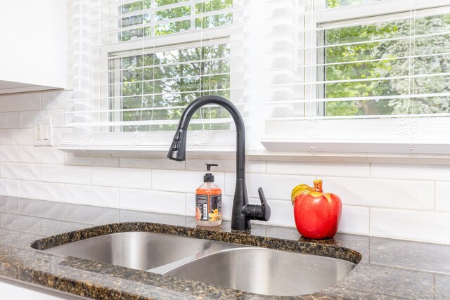 kitchen view of a sink, decorative backsplash, and dark stone countertops