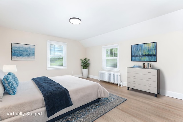 bedroom featuring radiator, light wood finished floors, baseboards, and lofted ceiling