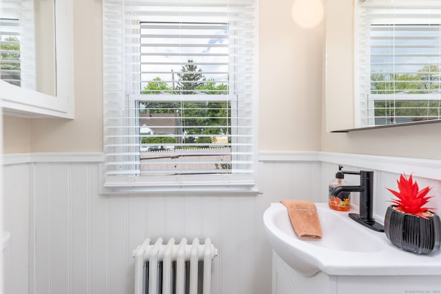 bathroom with radiator heating unit, wainscoting, plenty of natural light, a decorative wall, and a sink