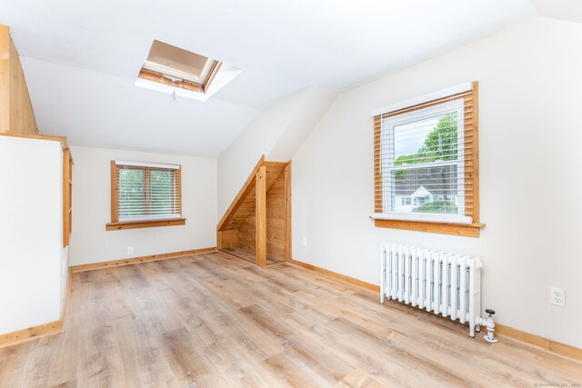 bonus room with radiator heating unit, a skylight, vaulted ceiling, wood finished floors, and baseboards