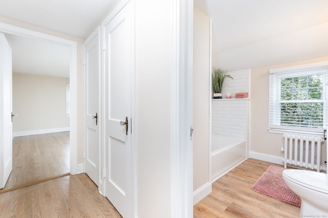 hallway featuring radiator heating unit, wood finished floors, and baseboards