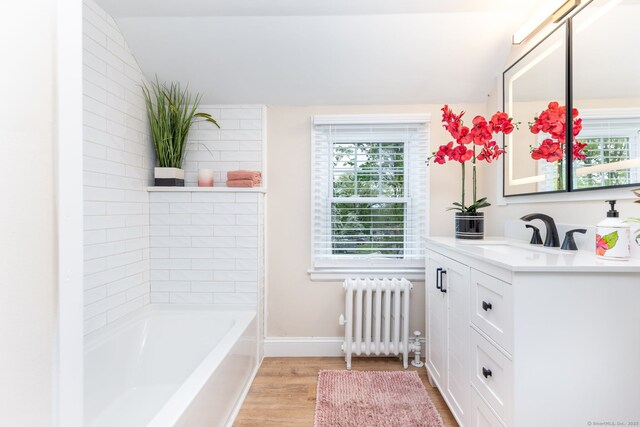 full bathroom featuring radiator, lofted ceiling, wood finished floors, a tub, and vanity