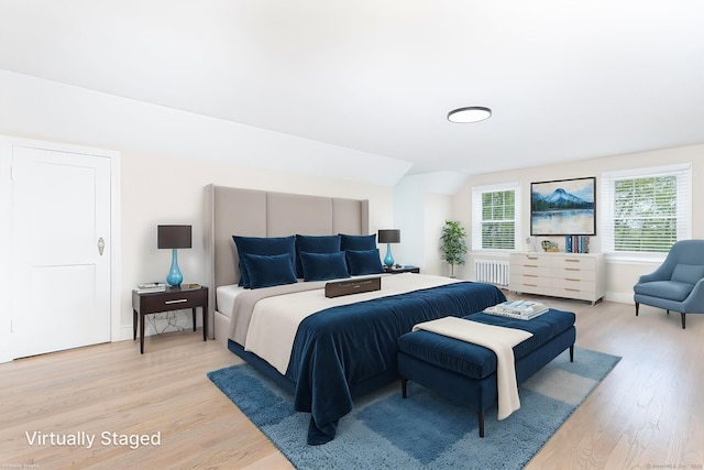bedroom with radiator, light wood-style flooring, baseboards, and lofted ceiling
