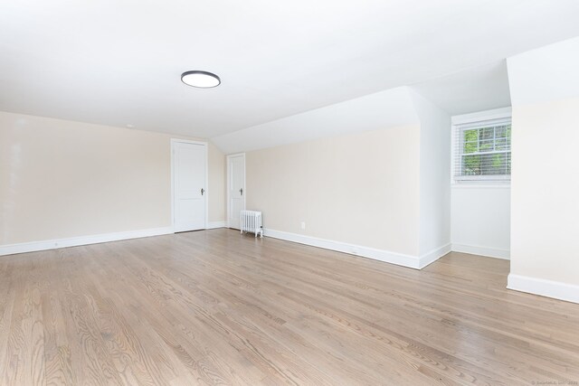 additional living space featuring radiator, light wood-type flooring, baseboards, and vaulted ceiling
