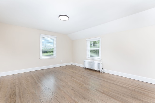 empty room featuring radiator, lofted ceiling, baseboards, and wood finished floors