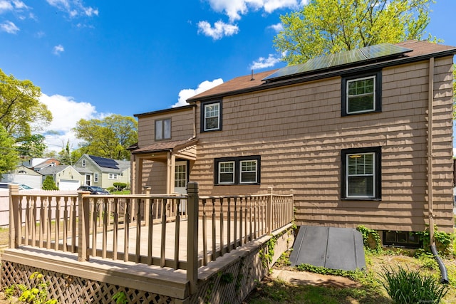 back of property with a wooden deck, roof mounted solar panels, and a residential view