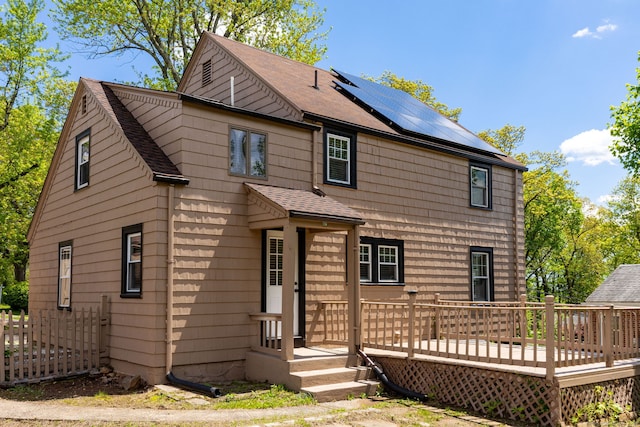 rear view of property featuring roof with shingles, roof mounted solar panels, and a deck