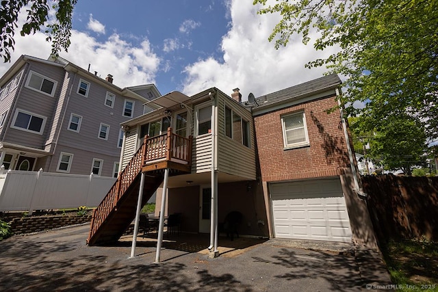 rear view of house featuring fence, a garage, stairway, brick siding, and a deck