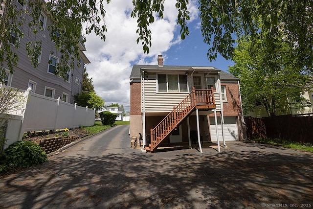 rear view of house with asphalt driveway, fence, stairway, and a chimney
