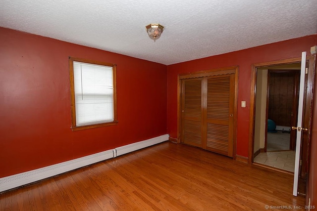 unfurnished bedroom with baseboard heating, wood finished floors, baseboards, a closet, and a textured ceiling