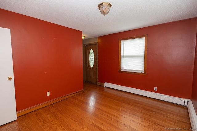 empty room with a baseboard heating unit, wood finished floors, baseboards, and a textured ceiling