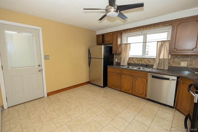 kitchen with stainless steel appliances, a sink, dark countertops, ceiling fan, and decorative backsplash