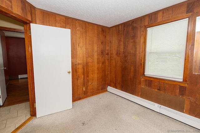 empty room featuring a baseboard radiator, wooden walls, a textured ceiling, and baseboard heating