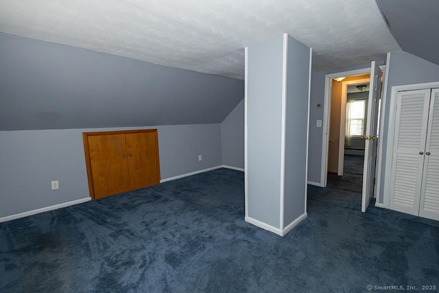 additional living space featuring baseboards, lofted ceiling, dark carpet, and a textured ceiling