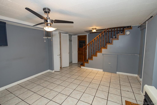 basement featuring a ceiling fan, stairs, baseboards, and light tile patterned floors