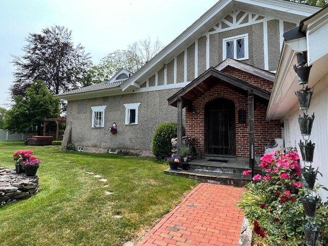 view of exterior entry featuring a lawn, brick siding, and stucco siding