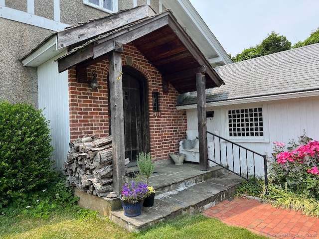 doorway to property with brick siding and roof with shingles