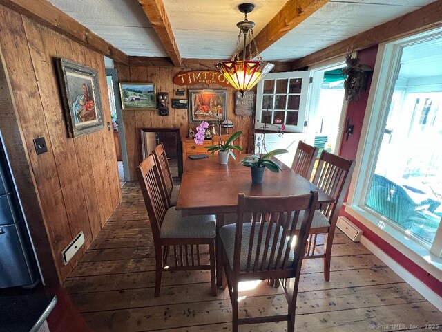 dining room featuring wooden walls, hardwood / wood-style floors, and beam ceiling
