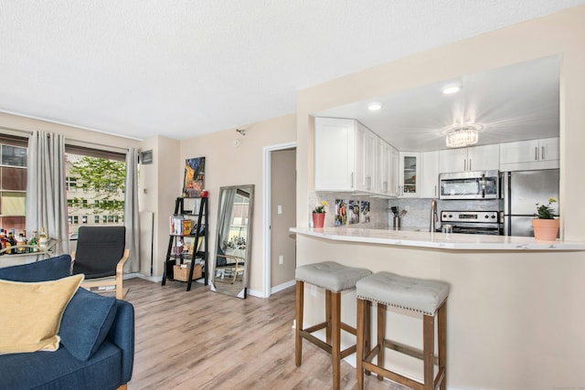 127 Greyrock Pl Unit 502, Stamford, CT 06901 - kitchen featuring stainless steel appliances, light wood-type flooring, white cabinets, decorative backsplash, and light countertops
