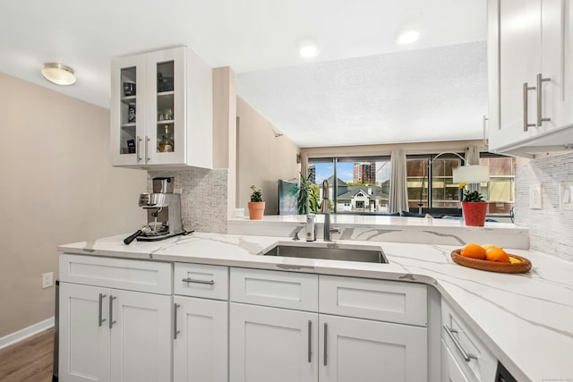 127 Greyrock Pl Unit 502, Stamford, CT 06901 - kitchen with backsplash, white cabinets, a sink, glass insert cabinets, and light stone countertops