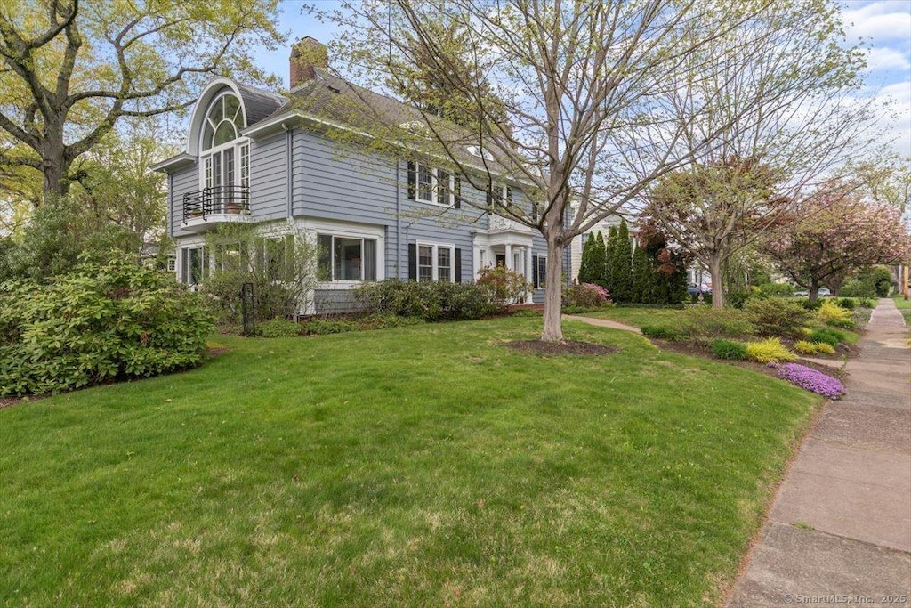 view of property exterior featuring a chimney, a lawn, and a balcony