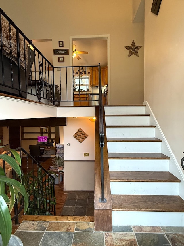 stairs featuring stone tile floors, a ceiling fan, and a high ceiling