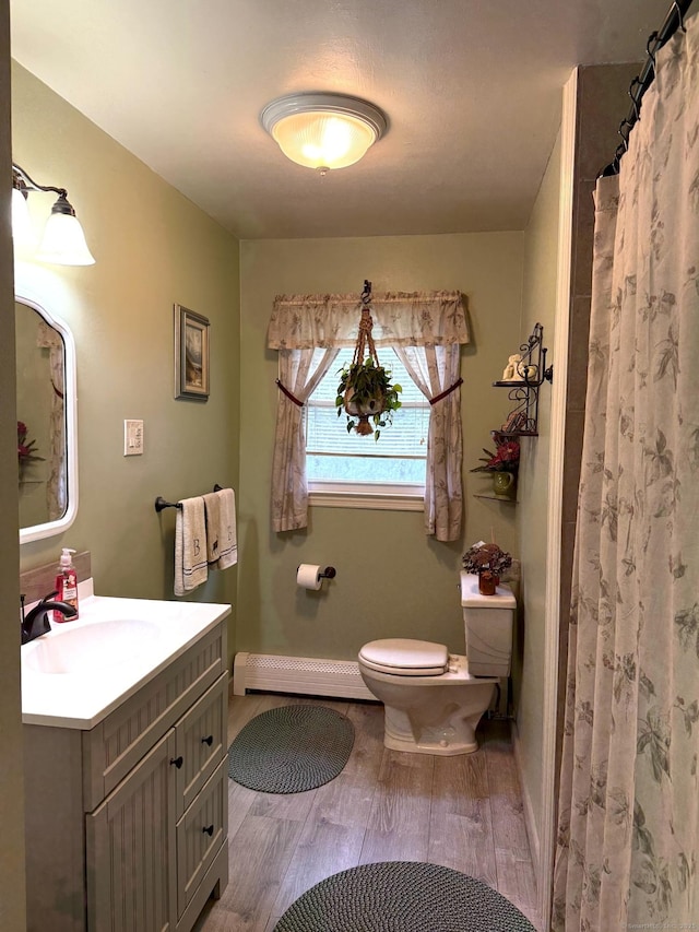 bathroom featuring baseboard heating, wood finished floors, toilet, vanity, and baseboards