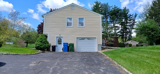 view of side of home with asphalt driveway, a lawn, a garage, and a wooden deck