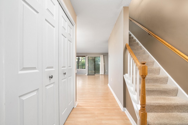 corridor with light wood finished floors, stairway, and baseboards