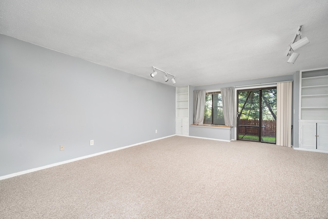 empty room featuring track lighting, carpet flooring, baseboards, built in features, and a textured ceiling