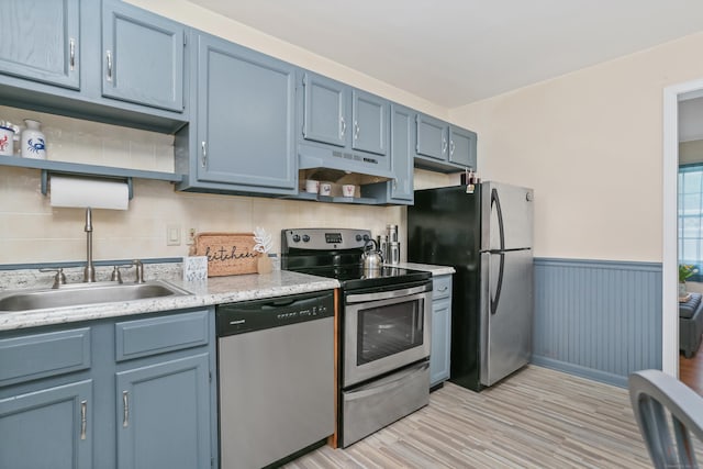 kitchen featuring stainless steel appliances, under cabinet range hood, blue cabinets, open shelves, and a wainscoted wall