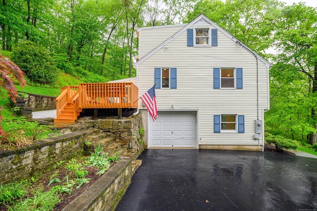 back of house with asphalt driveway, a wooden deck, and a garage
