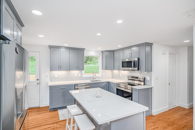 kitchen with stainless steel appliances, gray cabinetry, a sink, a kitchen breakfast bar, and backsplash