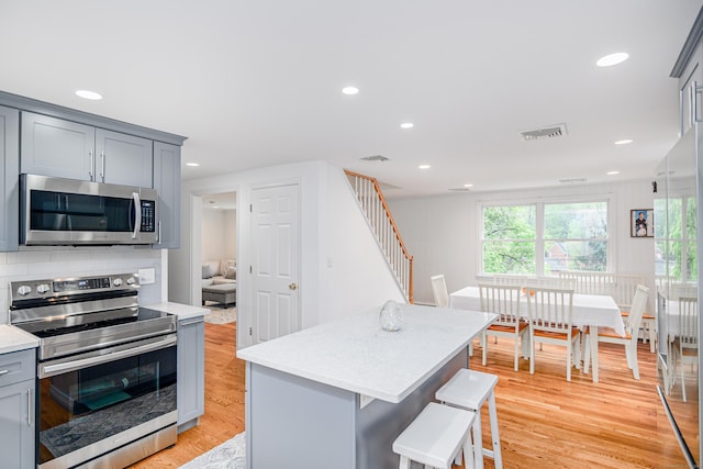 kitchen with appliances with stainless steel finishes, gray cabinetry, light countertops, light wood-style floors, and a kitchen bar