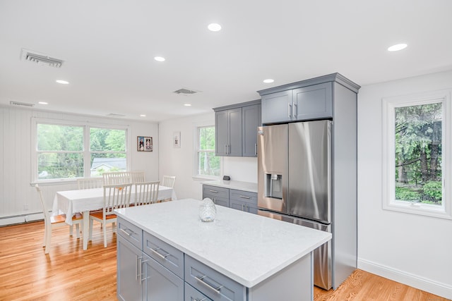 kitchen with stainless steel refrigerator with ice dispenser, gray cabinets, light countertops, light wood finished floors, and recessed lighting
