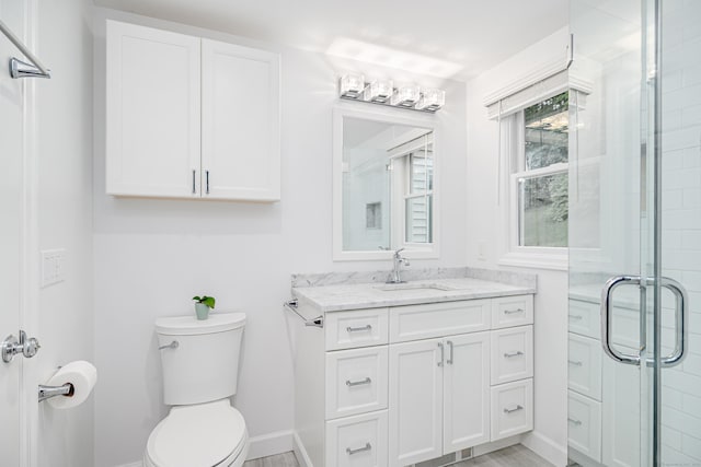 bathroom with toilet, a stall shower, vanity, and baseboards