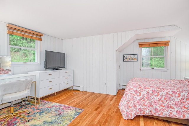 bedroom with light wood finished floors, baseboard heating, and wood walls