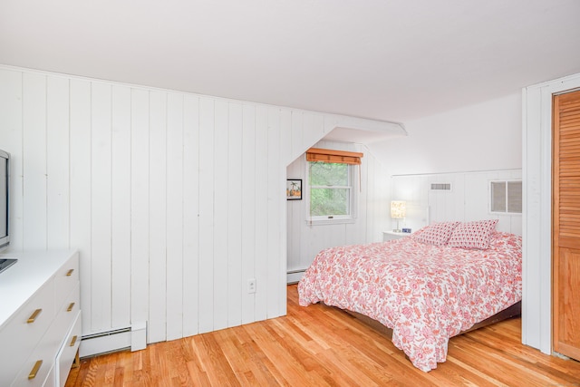 bedroom featuring a baseboard radiator, light wood finished floors, and wooden walls