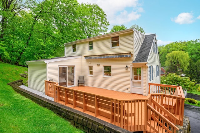 rear view of house featuring a wooden deck, a shingled roof, and a lawn