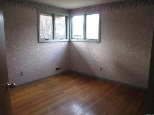 unfurnished room with baseboards, wood finished floors, and wallpapered walls
