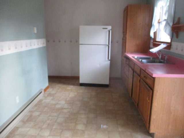 kitchen featuring freestanding refrigerator, a baseboard heating unit, a sink, and brown cabinetry