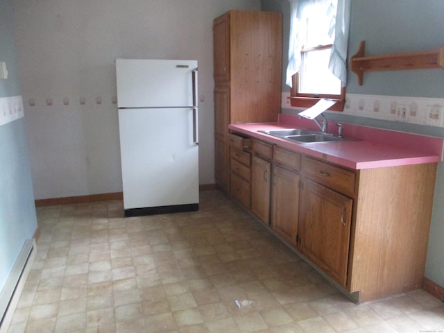 kitchen featuring freestanding refrigerator, a sink, brown cabinetry, light countertops, and light floors