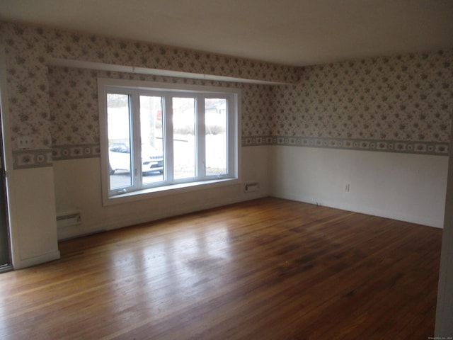 unfurnished room featuring wallpapered walls, a baseboard radiator, wood finished floors, and wainscoting