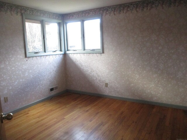 unfurnished room with baseboards, wood finished floors, and wallpapered walls