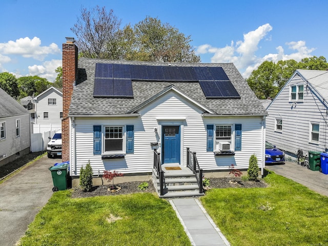 view of front of home featuring a shingled roof, a front yard, a chimney, and solar panels